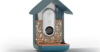 The Bird Buddy Pro smart bird feeder with an attached solar panel, mounted in a garden setting, capturing a bird.