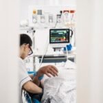Personnel médical aux urgences prenant en charge un patient, avec un thermomètre et un ventilateur en arrière-plan, symbolisant la lutte contre la canicule.
