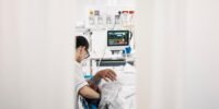 Personnel médical aux urgences prenant en charge un patient, avec un thermomètre et un ventilateur en arrière-plan, symbolisant la lutte contre la canicule.