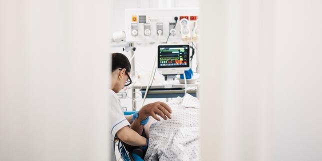 Personnel médical aux urgences prenant en charge un patient, avec un thermomètre et un ventilateur en arrière-plan, symbolisant la lutte contre la canicule.
