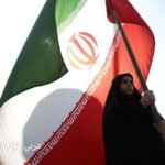تصعيد في الخليج وتفاهم وشيك: إسقاط مسيرة إيرانية ومفاوضات نووية مؤجلة 2 امرأة تحمل العلم الإيراني في أحد شوارع طهران، وسفن تجارية تعبر مضيق هرمز قبالة مسندم في عُمان.