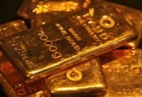 صورة لسبائك ذهبية متراكمة مع خلفية لسوق المال، تعكس تراجع أسعار الذهب العالمية.