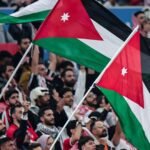 صورة توضيحية لشعار السفارة الأردنية في واشنطن مع خلفية لملعب كرة قدم، تعكس التنبيهات الصادرة للجماهير.