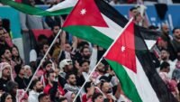 صورة توضيحية لشعار السفارة الأردنية في واشنطن مع خلفية لملعب كرة قدم، تعكس التنبيهات الصادرة للجماهير.