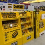 A collection of DeWalt yellow and black cordless power tools, including a drill, impact driver, and saw, displayed against a workshop background.