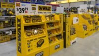 A collection of DeWalt yellow and black cordless power tools, including a drill, impact driver, and saw, displayed against a workshop background.