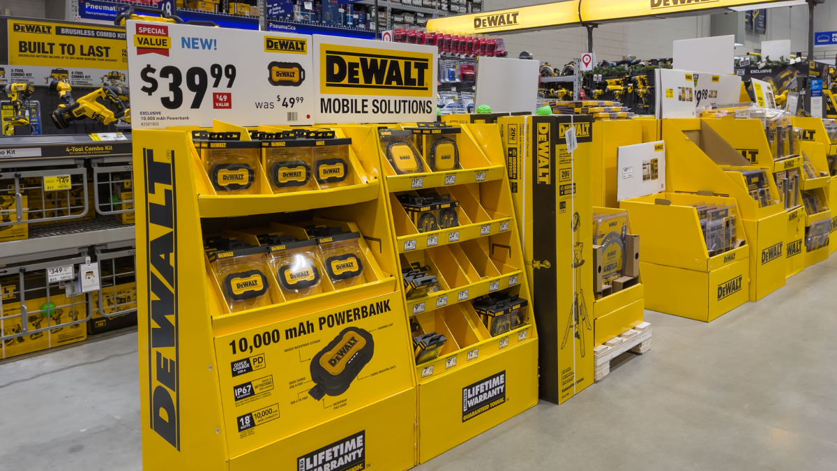 A collection of DeWalt yellow and black cordless power tools, including a drill, impact driver, and saw, displayed against a workshop background.