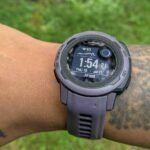 A fitness tracker worn on a tattooed wrist, showing a green light from its sensor.