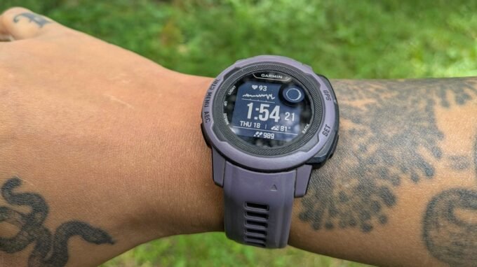 A fitness tracker worn on a tattooed wrist, showing a green light from its sensor.
