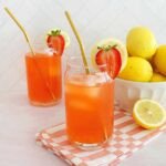 A pitcher and glasses of vibrant homemade strawberry lemonade with fresh strawberries and lemon slices.