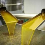Bouteilles d'huile d'olive marocaine de qualité supérieure sur un étal de marché européen, avec des olives vertes en arrière-plan, symbolisant la forte demande et l'augmentation des importations.