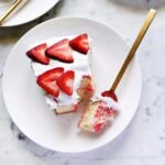 A vibrant Jello Poke Cake topped with white whipped cream and fresh berries, ready to be served.