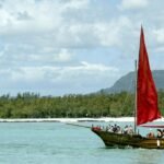 Jusqu’où Maurice peut-elle profiter de son modèle touristique ? 2 Vue aérienne d'une plage idyllique à l'île Maurice avec des cocotiers et des eaux turquoise, symbolisant le succès touristique mais aussi la fragilité environnementale.