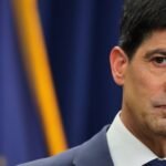 Kevin Warsh, the new Federal Reserve Chair, speaking at a press conference with a serious expression, symbolizing his firm stance on monetary policy.