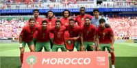 L'équipe nationale marocaine, les Lions de l'Atlas, en pleine discussion avec leur staff technique sur un terrain de football, symbolisant la préparation aux nouvelles règles de la FIFA pour la Coupe du Monde 2026.
