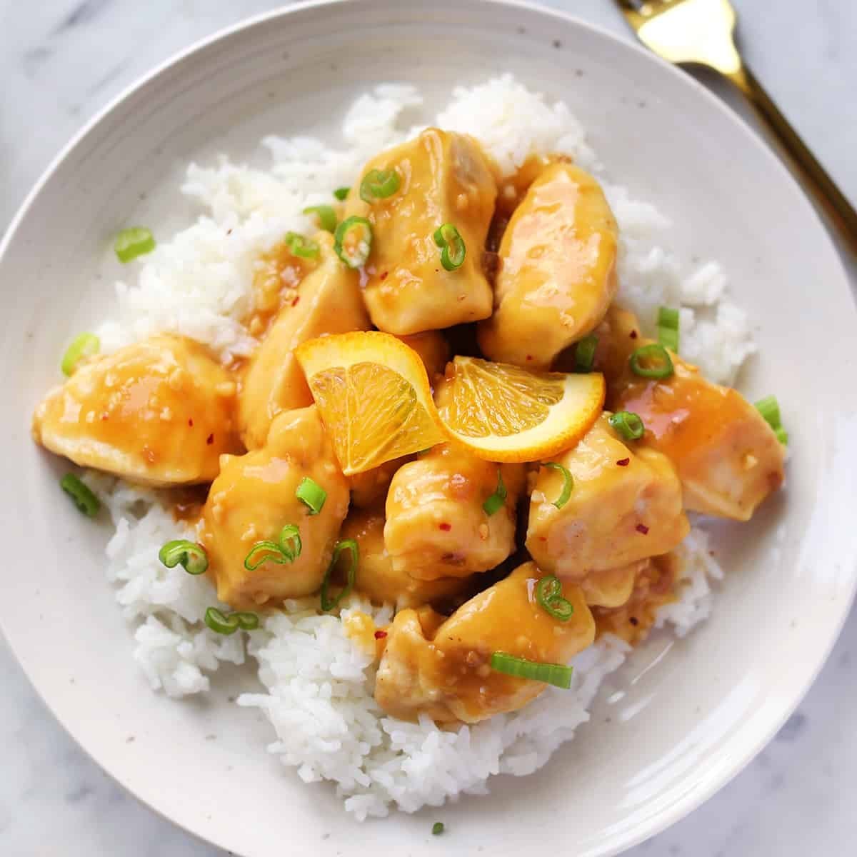 A vibrant bowl of homemade orange chicken sauce, garnished with fresh green onions, ready to be served.