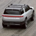 Rivian R2 SUV on a delivery truck, symbolizing the company's dual challenges of market launch and workforce restructuring.