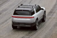 Rivian R2 SUV on a delivery truck, symbolizing the company's dual challenges of market launch and workforce restructuring.