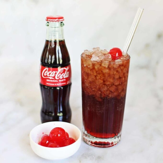 A vibrant Roy Rogers mocktail in a tall glass, garnished with a bright red maraschino cherry and ice.