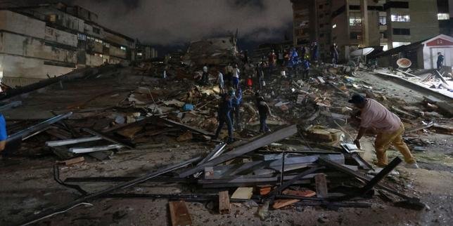 Vue aérienne de bâtiments endommagés après un séisme au Venezuela, avec des débris éparpillés et des équipes de secours en action.