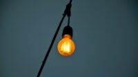 A smart light bulb glowing in a modern home setting, possibly with a smartphone controlling it.