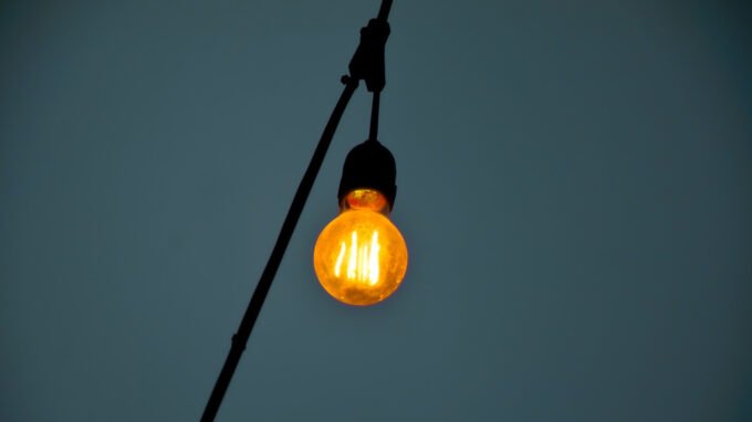 A smart light bulb glowing in a modern home setting, possibly with a smartphone controlling it.