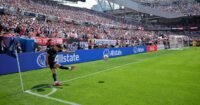 A soccer ball curving through the air towards a goal, with a blurred background of a stadium.