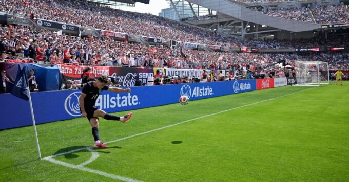 A soccer ball curving through the air towards a goal, with a blurred background of a stadium.