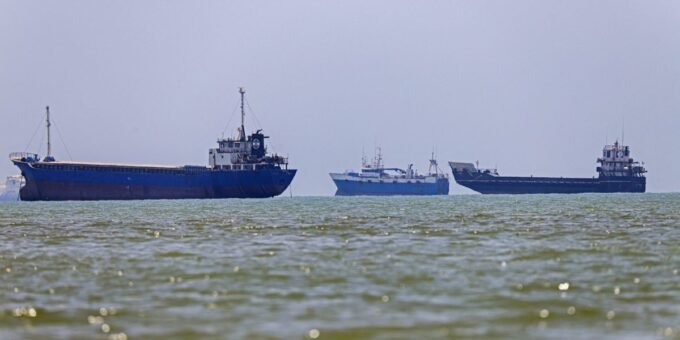 Oil tanker navigating the Strait of Hormuz with a backdrop of a clear sky and distant land