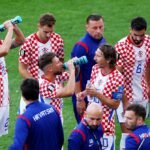 Football players taking a hydration break during a World Cup match, with advertising hoardings visible.
