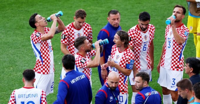 Football players taking a hydration break during a World Cup match, with advertising hoardings visible.