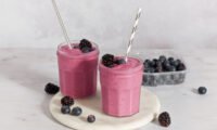 Vibrant berry pie smoothie in a glass, surrounded by fresh berries, spinach, and cauliflower, ready to be blended.