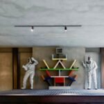A modern Brutalist home interior in Milan featuring exposed concrete, a sculptural staircase, and contemporary art.