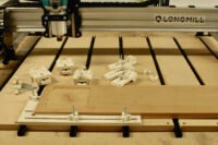 Two types of DIY CNC workholding clamps made from plywood, securing a workpiece on a CNC router bed.