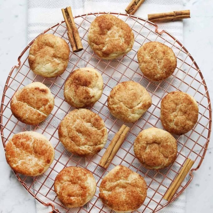 The Ultimate Cream of Tartar-Free Snickerdoodle: Soft, Chewy & Irresistible 7 A plate of golden-brown, soft, and chewy snickerdoodle cookies coated in cinnamon sugar, with some dough balls ready for baking.