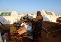 امرأة نازحة تقف أمام صندوق كرتوني فارغ في مخيم للنازحين بمدينة الأبيض، السودان، في مشهد يعكس الأزمة الإنسانية المتفاقمة.