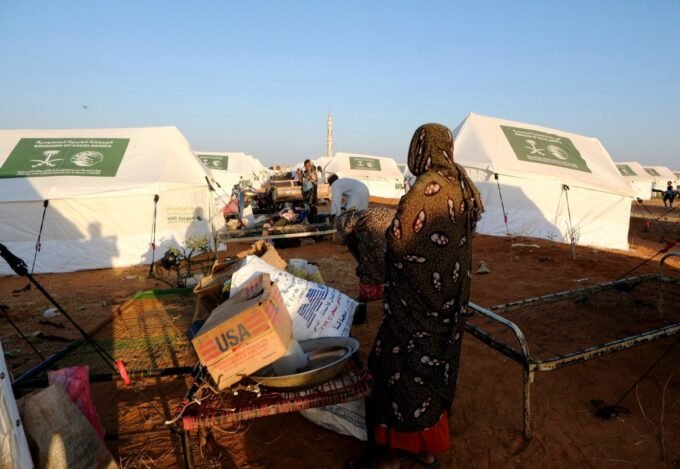 امرأة نازحة تقف أمام صندوق كرتوني فارغ في مخيم للنازحين بمدينة الأبيض، السودان، في مشهد يعكس الأزمة الإنسانية المتفاقمة.