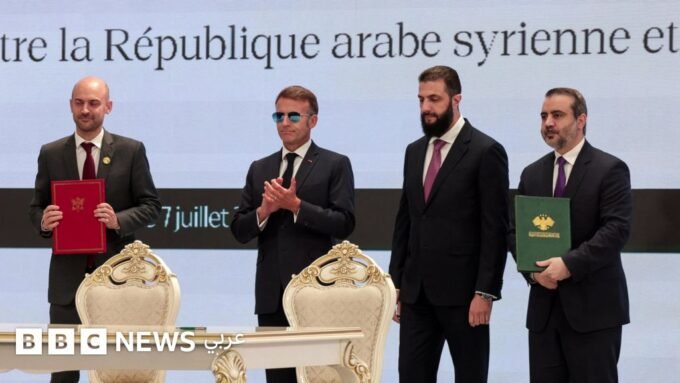 صورة تظهر الرئيس الفرنسي إيمانويل ماكرون والرئيس السوري أحمد الشرع خلال مؤتمر صحفي في دمشق، مع خلفية لعلمي البلدين.