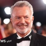 صورة للممثل سام نيل في حفل جوائز، يبتسم وهو ينظر إلى الجمهور.