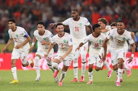 صورة تجمع لاعبي المنتخب المغربي يحتفلون بفوزهم في كأس العالم، مع شعار كأس العالم 2026 في الخلفية.
