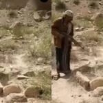 شاب يمني يحمل بندقية ويطلق النار على قبر في منطقة جبلية، تعبيرًا عن غضبه من نزاع على الميراث.
