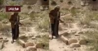 شاب يمني يحمل بندقية ويطلق النار على قبر في منطقة جبلية، تعبيرًا عن غضبه من نزاع على الميراث.
