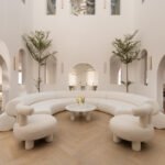 A bright, open central courtyard of The White Arcade luxury home in Dubai, featuring layered white arches, a glass roof, mature trees, and a curved bespoke sofa.