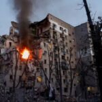 Des secouristes ukrainiens et des civils inspectent les dégâts causés par des frappes de missiles russes sur des bâtiments résidentiels et des infrastructures à Kiev, avec de la fumée s'élevant dans le ciel.