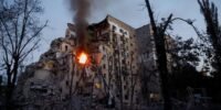 Des secouristes ukrainiens et des civils inspectent les dégâts causés par des frappes de missiles russes sur des bâtiments résidentiels et des infrastructures à Kiev, avec de la fumée s'élevant dans le ciel.