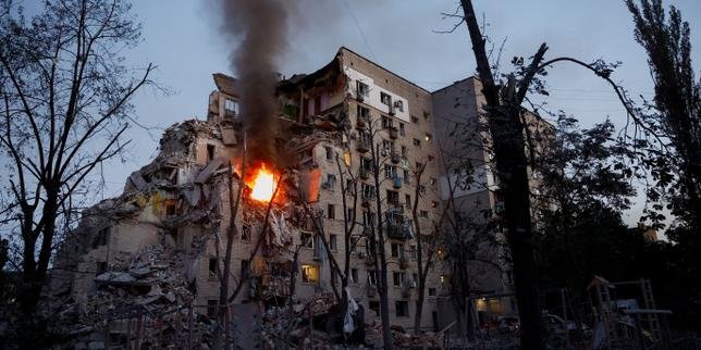 Des secouristes ukrainiens et des civils inspectent les dégâts causés par des frappes de missiles russes sur des bâtiments résidentiels et des infrastructures à Kiev, avec de la fumée s'élevant dans le ciel.