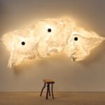 Erwan Bouroullec's Maap: A Revolutionary Wall Lamp Designed for Personal Expression 8 Erwan Bouroullec's Maap wall lamp, showcasing a crumpled Tyvek diffuser secured by magnetic dots on a steel framework, casting a soft, ambient glow on a wall.