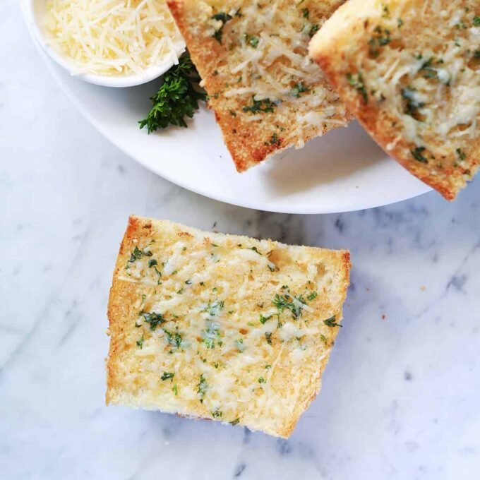 Crispy golden garlic toast slices on a baking sheet, garnished with fresh parsley.