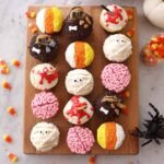 A festive spread of various Halloween-themed food and drinks, including cupcakes, jello shots, and pumpkin treats.