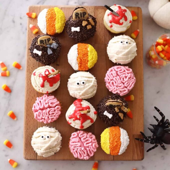 A festive spread of various Halloween-themed food and drinks, including cupcakes, jello shots, and pumpkin treats.